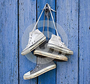 Two pairs of old worn textile sneakers hang on a nail