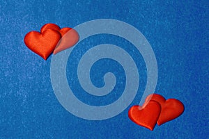 Two pairs of red hearts on cardboard background of classic blue color