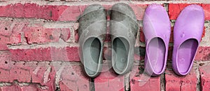 Two pairs of rubber galoshes in black and pink on the background of an old brick wall, a copy of the space on the left