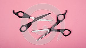 Two pairs of scissors for haircuts on a pink background