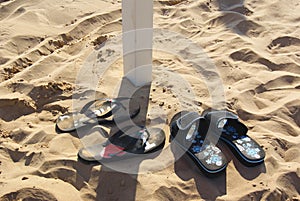 Two pairs of slippers flip-flops sprinkled sand beach.