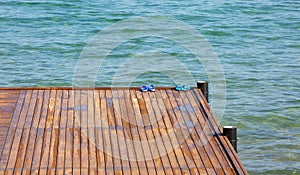 Two pairs of slippers stand on a wooden pantone against the backdrop of a beautiful clear sea.