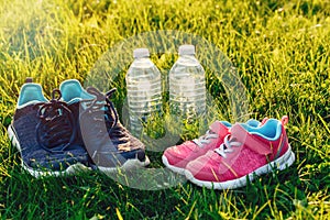 Two pairs of sneakers and bottles of water in green grass outside on sunset