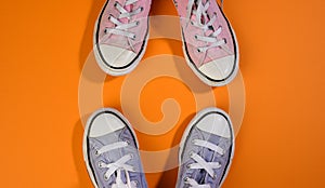 Two pairs of textile sneakers on an orange background stand opposite each other. Dialogue and confrontation concept