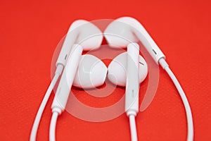 Two pairs of white headphones close to each other on red background, one pair of earphones is blurred
