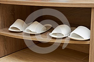 Two pairs of white open-toed slippers stand in a shoe cabinet