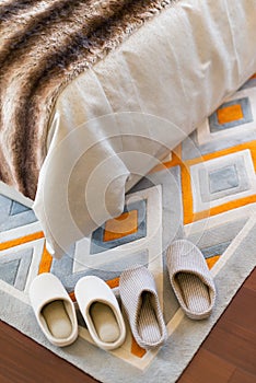 Two pairs of white slippers on carpet near a bed