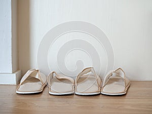 Two pairs of white soft slippers on wooden floor on white wall background