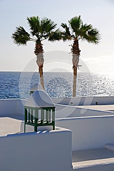 Two palm trees against the sun with white wash building & sea ocean water horizon at Puerto Del Carmen, Lanzarote, Spain