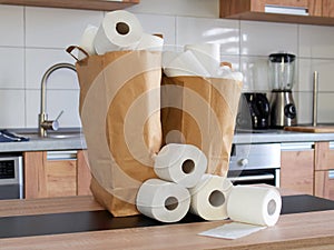 Two paper bags full of rolls of toilet paper standing on the kitchen table. Stock shopping. Lots of toilet paper.