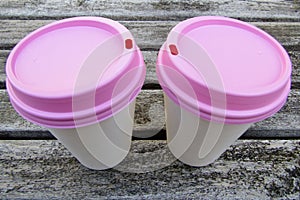 Two paper coffee cups with pink lids on wooden table