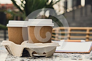 Two paper cups with lid for tea to go. Coffee take away on the table. Take-out coffees with brown paper cup holder