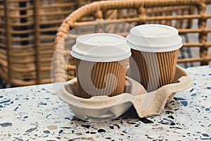 Two paper cups with lid for tea to go. Coffee take away on the table. Take-out coffees with brown paper cup holder