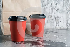 Two paper cups for tea or coffee to go and takeaway craft bag on gray background copy space. Concept for the development of the