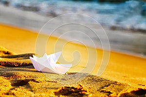 Two paper white ships on the sand near the sea.White crafts origami handmade on the beach on a background of waves