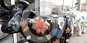 Two papier mache cow statues with painted flowers in front of the butchers shop