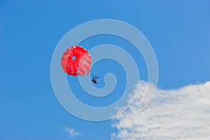 Two people under red parachute flying over the blue sky