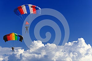 Two parachutists soar on colorful parachutes across the boundless blue sky against the background of white fluffy clouds