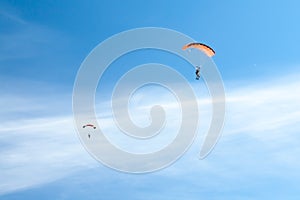 Two parachutists soar on colorful parachutes across the boundless blue sky against the background of white fluffy clouds