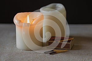 Two paraffin candles burn in the dark, as an alternative sources of light and heat. Blackout and energy crisis concept.