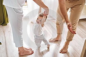 Two parents teaching their baby to perform first steps