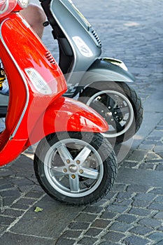 Two parked red and gray scooters on a cobblestone street.
