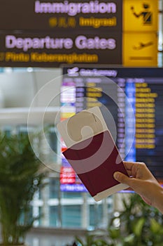 Two passports and boarding passes in a woman hand opposite the information board for departure and arrival inside an airport