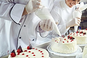 Two pastry chefs decorate a cake from a bag in a pastry shop photo