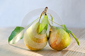 Two pears on one stalk with leaves. With drops of water, lit by the sun on wooden background. Paired fruits