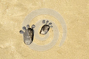 Two pebble footprints on the surface of the desert sea sand. Games on the sand and on the beach. A copy of the space