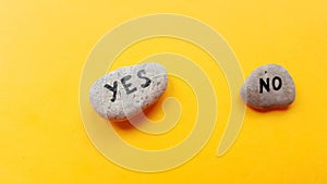 Two pebbles with yes and no text on orange table