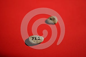 Two pebbles with yes and no text on them. Red sunny table. Focus on yes