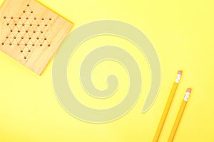 Two pencils and a gameboard lie together against a yellow background, as if balancing on a see-saw.