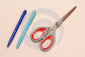 Two pens and scissors on a beige background