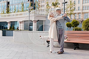 Two pensioners dance on the square near the bench. They are happy