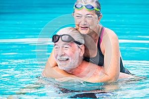 Two pensioners or mature old people enjoying summer and vacations in the swimming pool together having fun smiling and laughing -