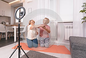 two pensioners are sitting on the bedroom floor in front of a tripod for the camera, shooting a fitness video tutorial