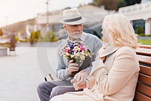 Two pensioners are sitting on a bench in the alley. An elderly man gives a woman flowers