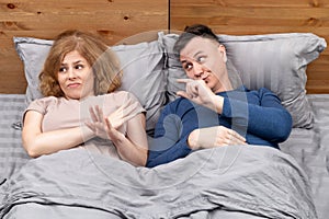 Two people in bed, a begging man shows his fingers to a woman who ignores him how much he needs.