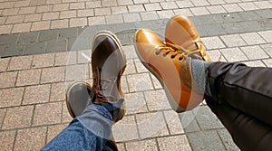 Two People Crossing Legs Wearing Boots in the Middle of the Day