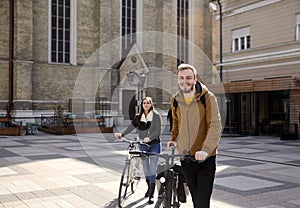 Two people - friends or couple, pushing their bicycles in a old city square in Europe, Serbia, Novi Sad. Smiling