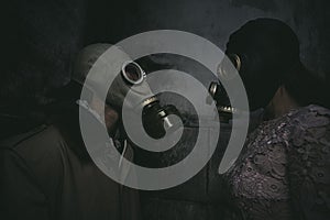 two people in gas masks stand against a wall in a small dark room and look at each other