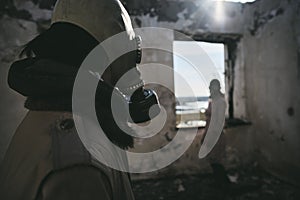 Two people, a guy and a girl in gas masks, stand inside an abandoned house