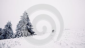 Two people hike up the mountain in deep snowy and misty winter landscape