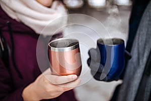 Two people hold thermo mugs with hot steaming tea