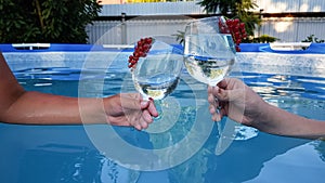 two people are holding glasses with alcoholic refreshing summer cocktail close-up on the background of the pool. the
