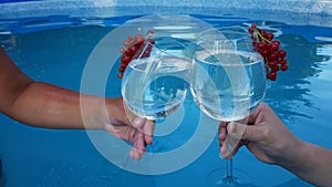 two people are holding glasses with alcoholic refreshing summer cocktail close-up on the background of the pool. the