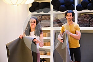 Two people are holding a yoga mat in a room with shelves full of yoga material.