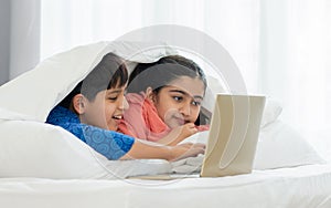 Two people, Indian teenage brother, sister smiling, using laptop to online learning, do homework, watching movie together with fun