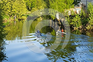 Two people are kayaking along the city river on a sunny day